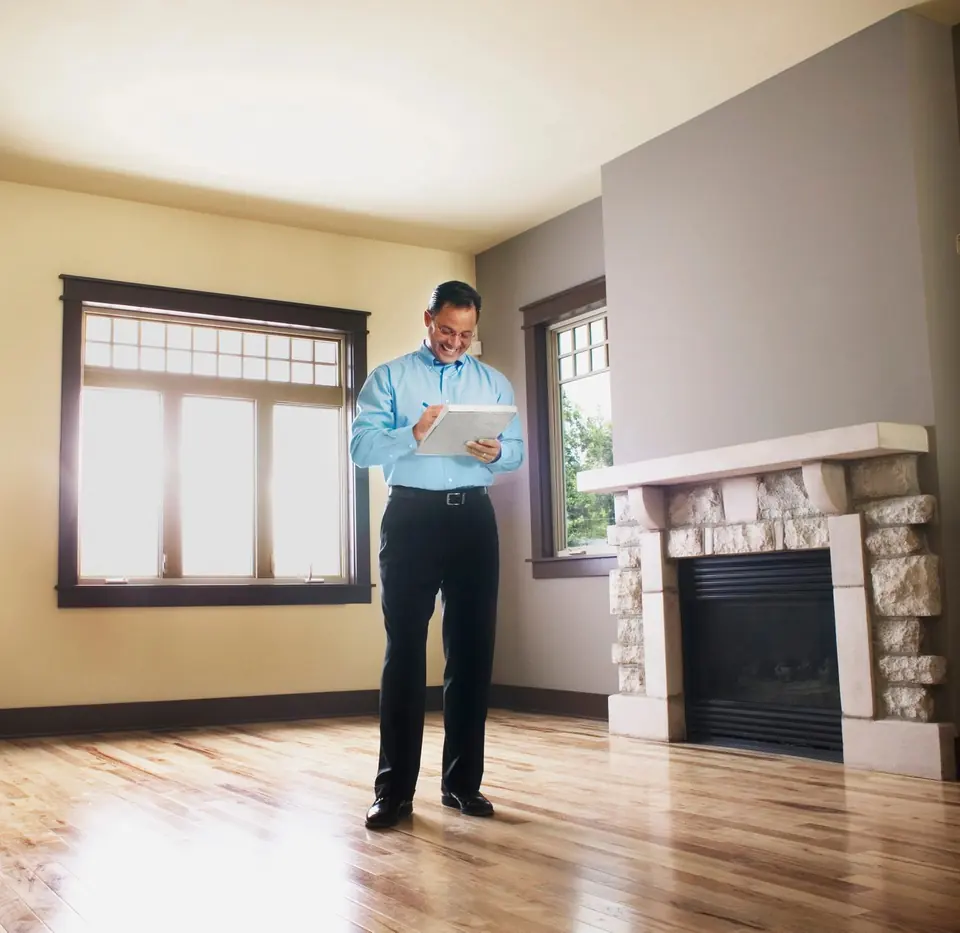 A home inspector checking a tablet in the empty living room of a house