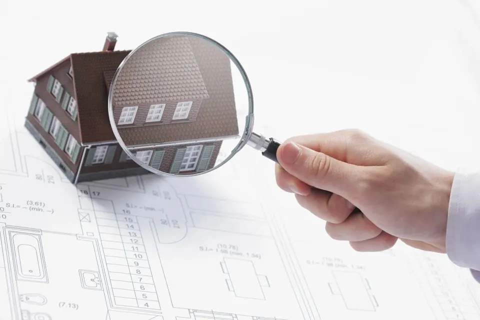 A magnifying glass held over a model house standing on a set of floor plans